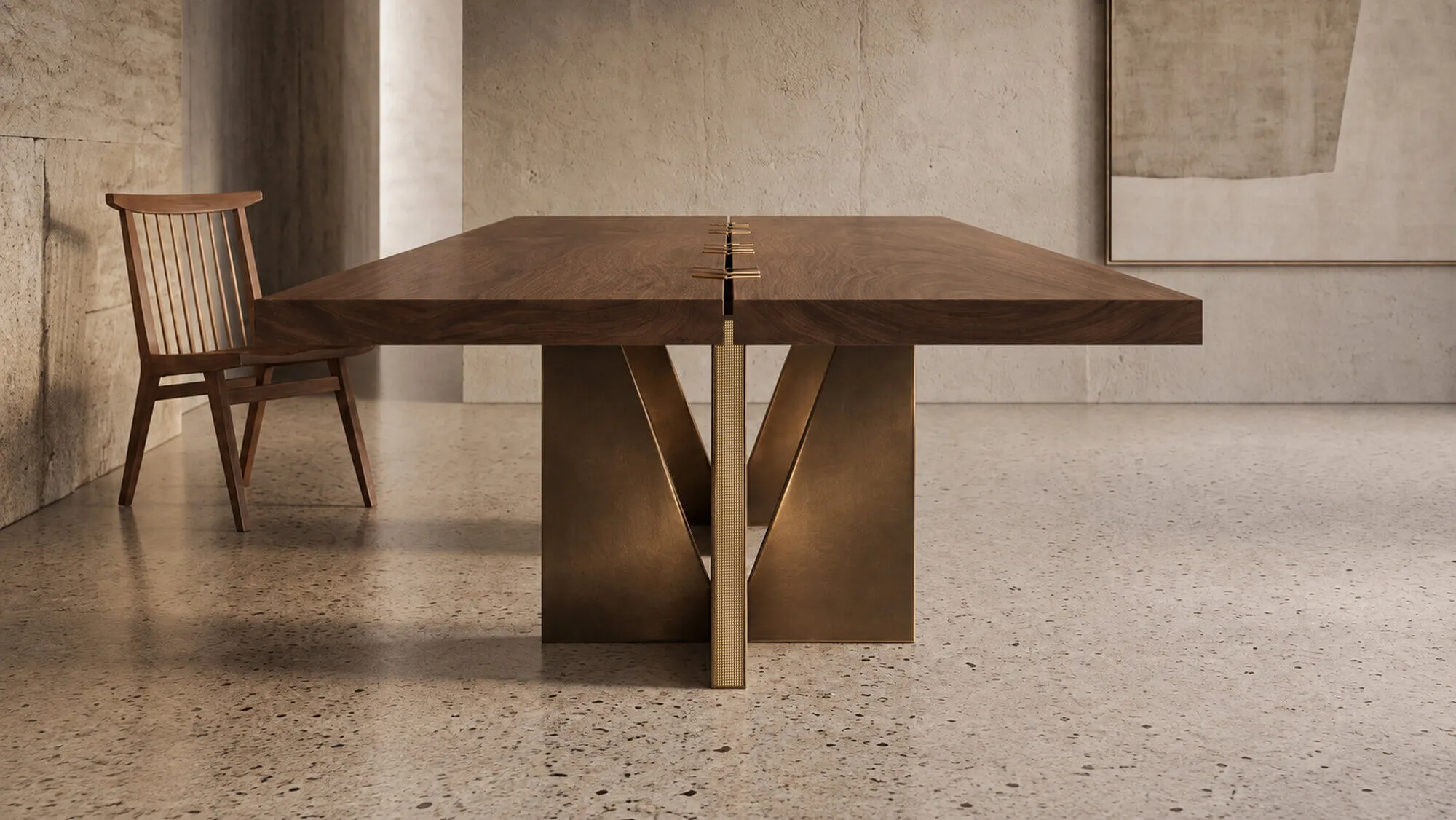 The AURUM table seen from its end in a stone room: a solid walnut top on bronze and brass bases, a wooden chair beside it
