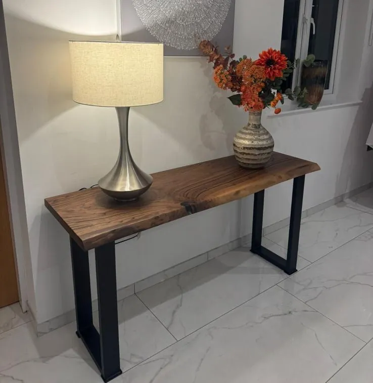 A walnut console table with a lamp and a vase of flowers against a white wall