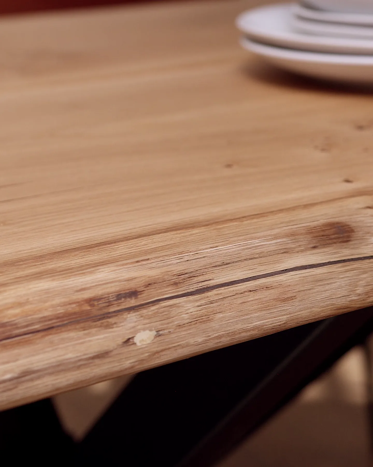 Il bordo naturale di un piano in rovere da vicino, con i nodi e una sottile crepa conservati e i piatti sfocati sullo sfondo